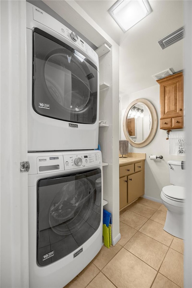 half bathroom with estacked washer and dryer, toilet, tile patterned flooring, and vanity