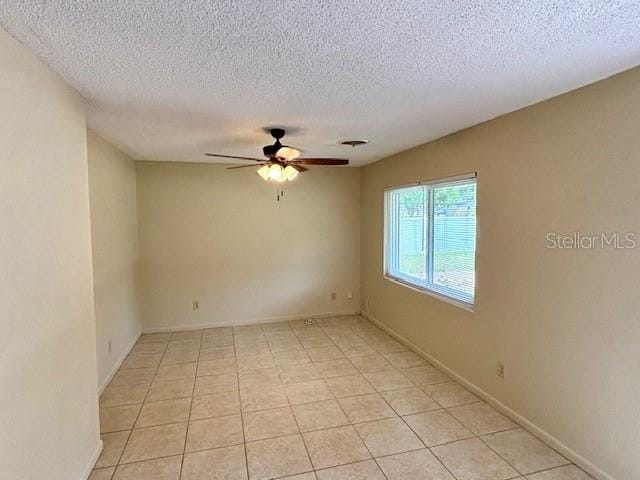 empty room with ceiling fan, a textured ceiling, light tile patterned floors, and baseboards