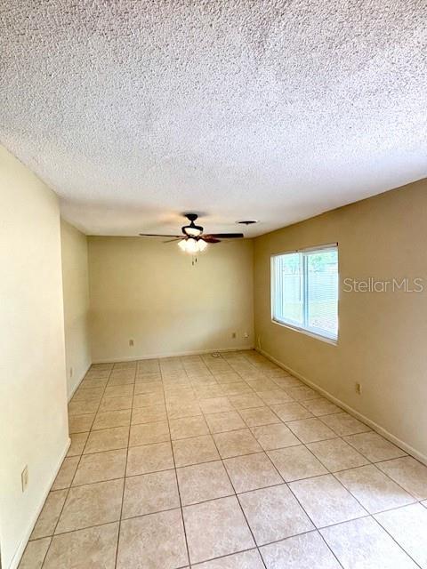 empty room with a ceiling fan, a textured ceiling, and light tile patterned flooring