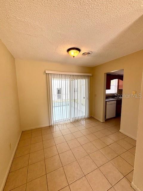 empty room featuring a textured ceiling, light tile patterned flooring, and baseboards