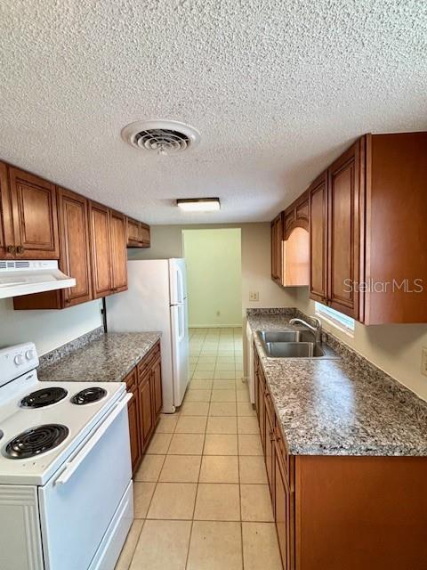 kitchen with white appliances, range hood, a sink, brown cabinetry, and light tile patterned floors