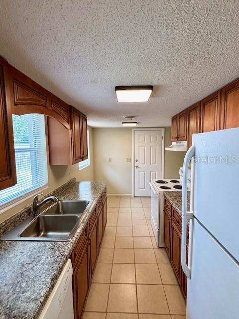 kitchen featuring white appliances, a sink, brown cabinetry, under cabinet range hood, and light tile patterned floors