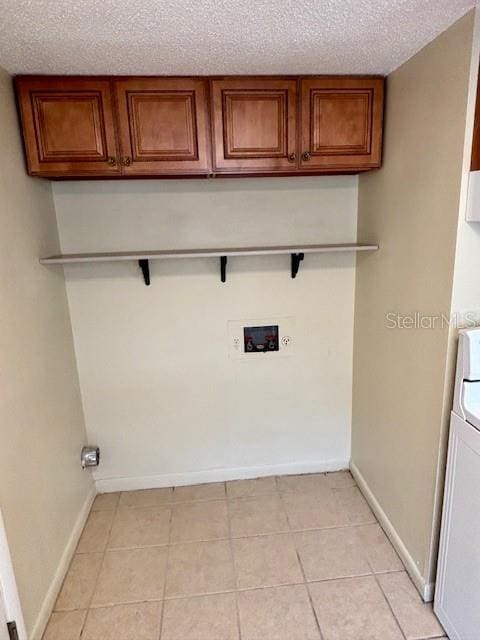 clothes washing area with cabinet space, baseboards, light tile patterned flooring, and a textured ceiling