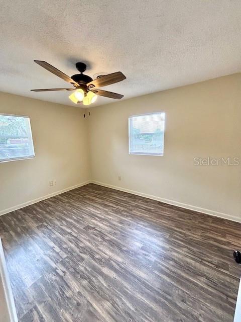 spare room featuring plenty of natural light, dark wood-type flooring, a textured ceiling, and baseboards