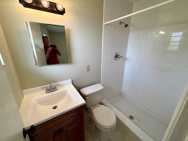 bathroom with toilet, tiled shower, vanity, and tile patterned flooring