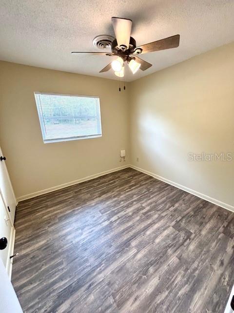 empty room with a textured ceiling, a ceiling fan, dark wood-style flooring, and baseboards
