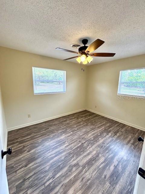 spare room with healthy amount of natural light, a textured ceiling, wood finished floors, ceiling fan, and baseboards