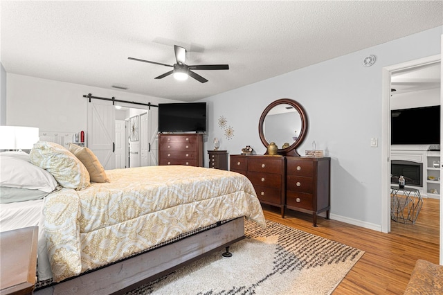 8874 SW 95th St Unit E, Ocala, FL 34481 - bedroom with wood finished floors, a barn door, a textured ceiling, ceiling fan, and baseboards