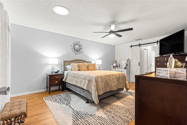 8874 SW 95th St Unit E, Ocala, FL 34481 - bedroom featuring a barn door, light wood-style floors, a textured ceiling, baseboards, and ceiling fan