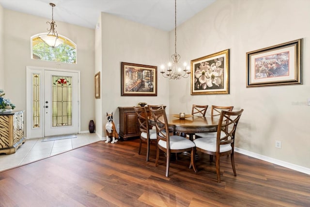 dining area featuring wood finished floors, a chandelier, baseboards, and a towering ceiling