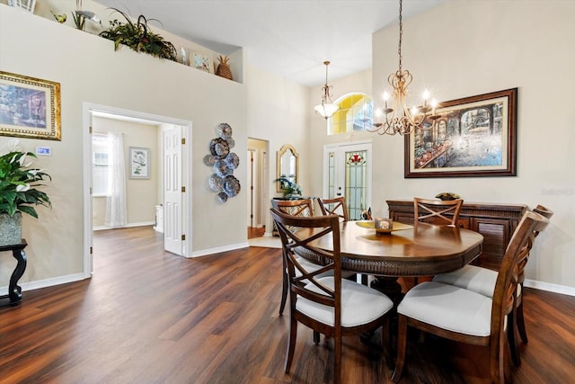 dining space with dark wood-type flooring, a chandelier, baseboards, and a towering ceiling