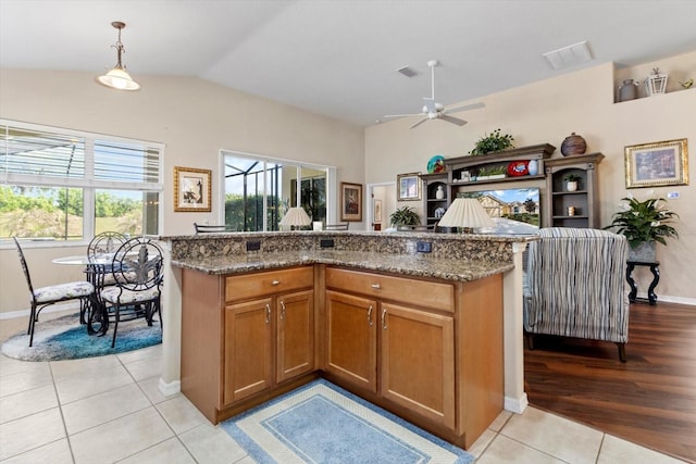 kitchen with light tile patterned flooring, a ceiling fan, dark stone counters, brown cabinets, and vaulted ceiling