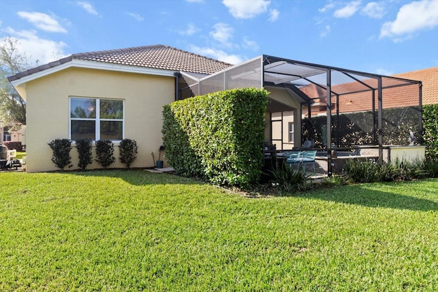 rear view of house featuring stucco siding, a tiled roof, a lawn, and glass enclosure