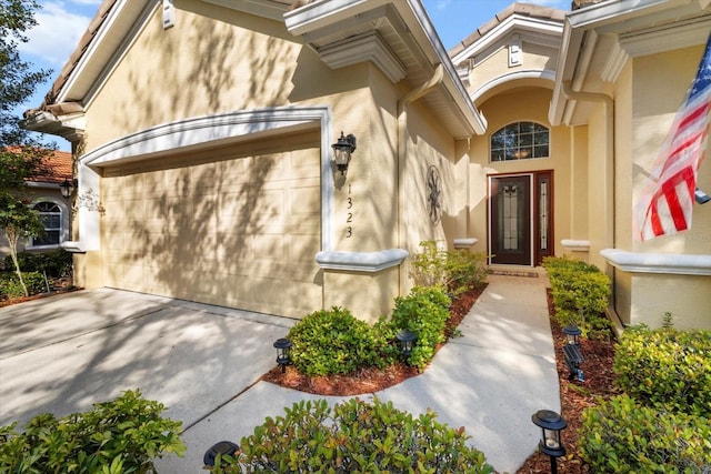 doorway to property with an attached garage, stucco siding, and concrete driveway