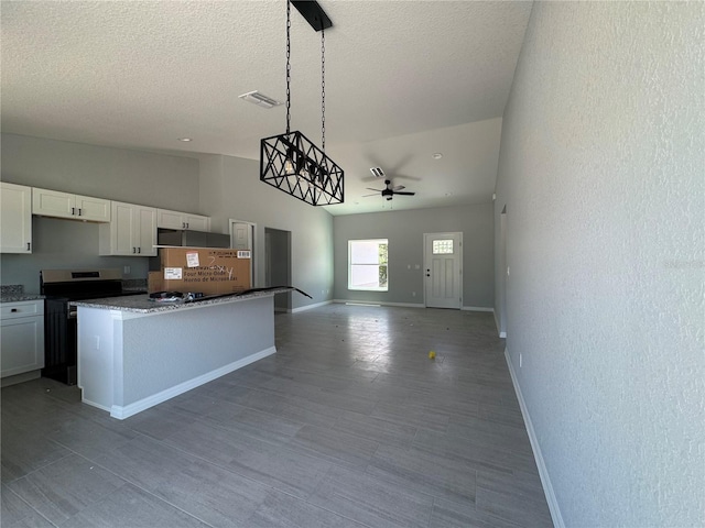 kitchen featuring stainless steel electric range, baseboards, white cabinetry, ceiling fan, and a center island