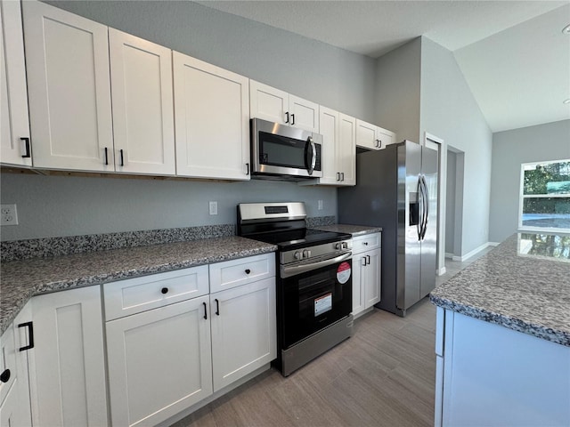 kitchen featuring stainless steel appliances, lofted ceiling, light wood finished floors, white cabinetry, and dark stone countertops