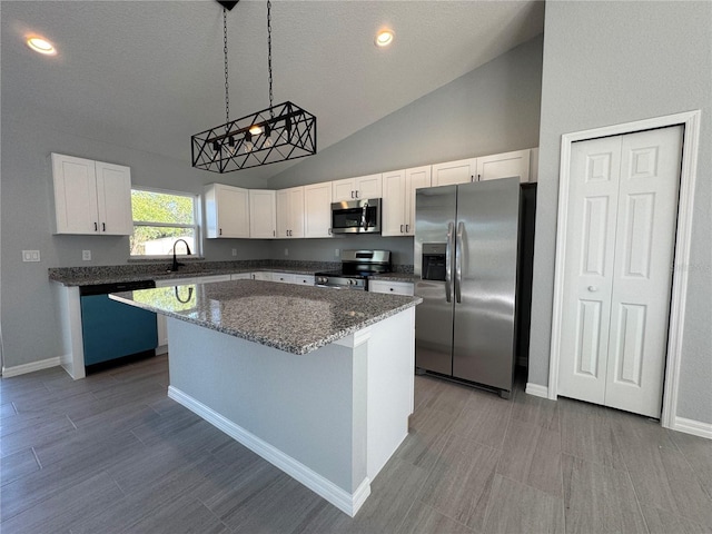kitchen featuring appliances with stainless steel finishes, a kitchen island, white cabinets, vaulted ceiling, and hanging light fixtures