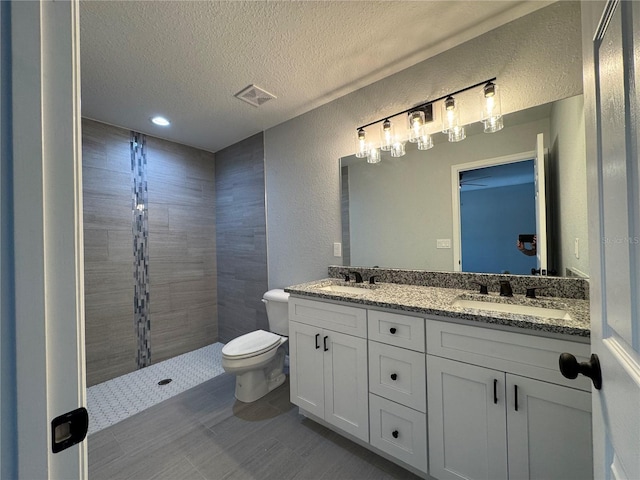 bathroom featuring a textured ceiling, double vanity, toilet, tiled shower, and a textured wall