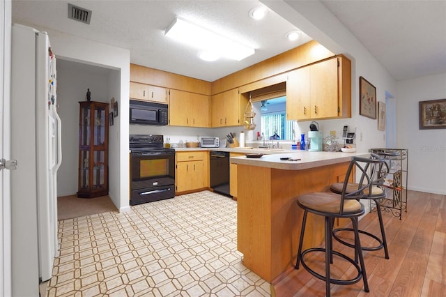 kitchen featuring black appliances, a peninsula, light countertops, a breakfast bar, and a sink