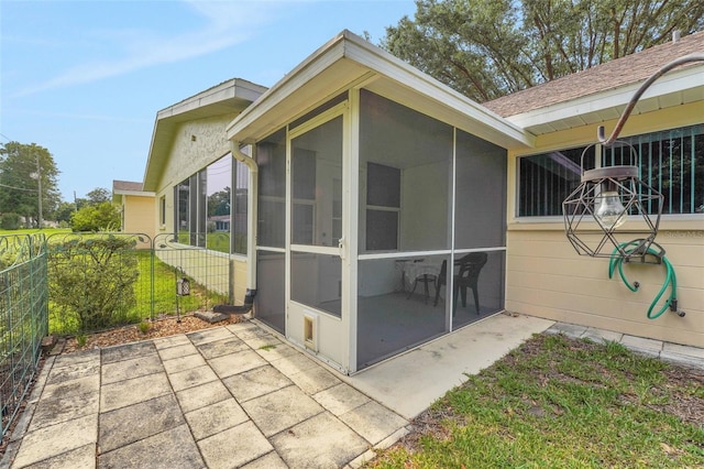 view of home's exterior featuring a sunroom, fence, a patio area, and roof with shingles
