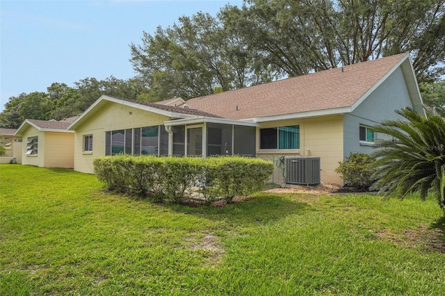rear view of house with central air condition unit, a sunroom, a lawn, and a shingled roof