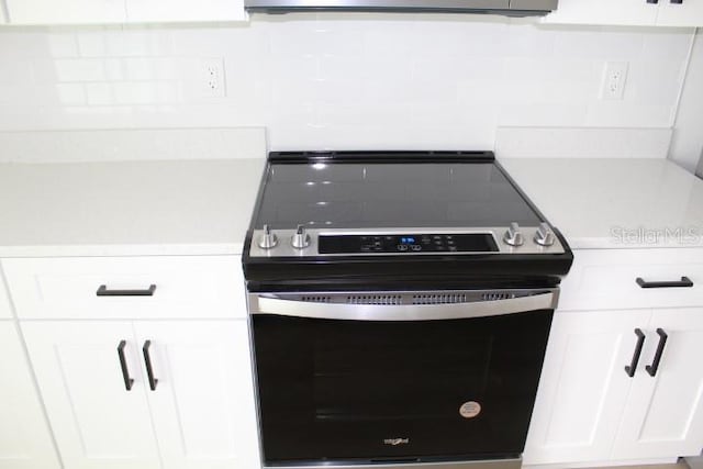 kitchen view of range with electric cooktop, white cabinets, light countertops, and backsplash