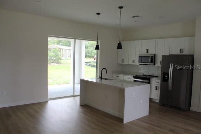 kitchen featuring appliances with stainless steel finishes, a sink, wood finished floors, white cabinets, and backsplash