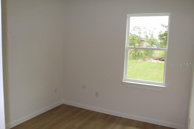 unfurnished room featuring baseboards, wood finished floors, and healthy amount of natural light