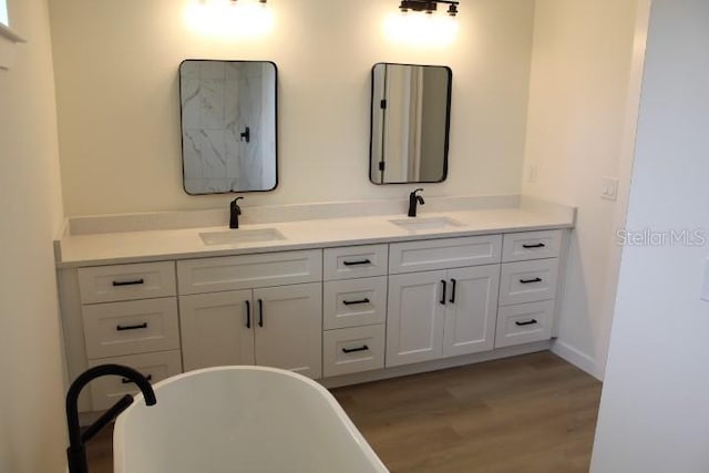 bathroom featuring wood finished floors, double vanity, and a soaking tub