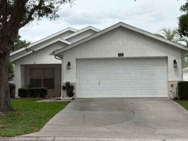 ranch-style home featuring stucco siding, concrete driveway, a garage, a front lawn, and brick siding