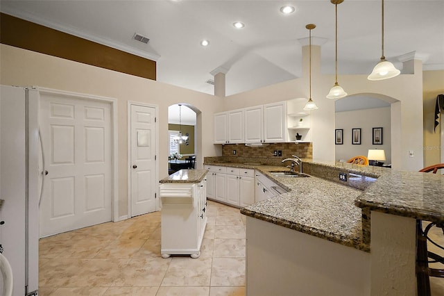kitchen with freestanding refrigerator, a sink, arched walkways, stone counters, and open shelves