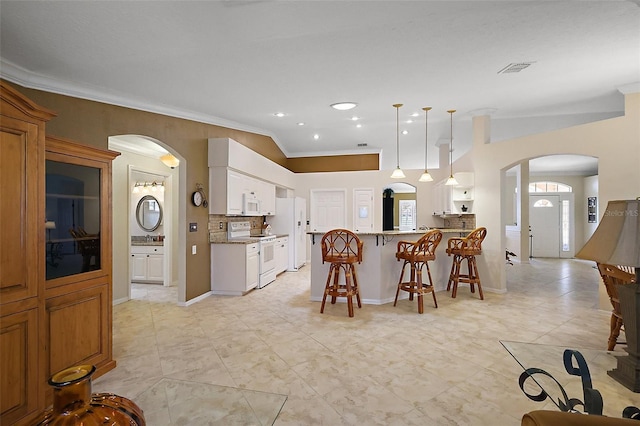 kitchen featuring white appliances, arched walkways, a kitchen bar, a peninsula, and crown molding