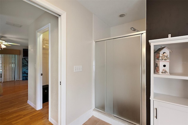 full bath with a stall shower, a ceiling fan, wood finished floors, a spacious closet, and baseboards
