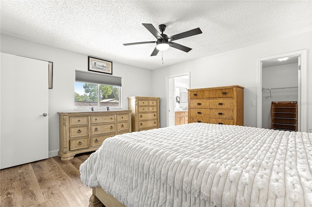 bedroom featuring light wood-style flooring, a textured ceiling, ensuite bath, and a ceiling fan