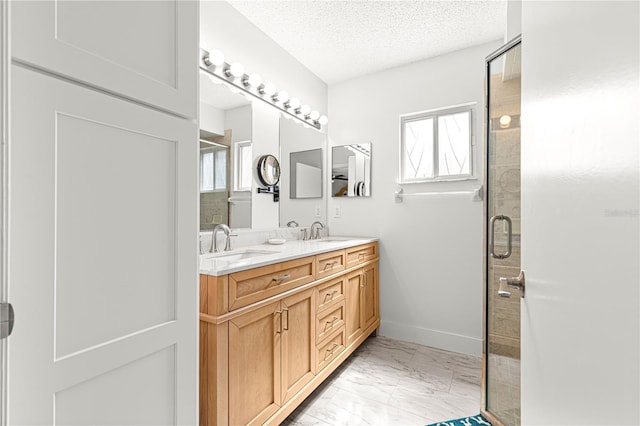 bathroom featuring marble look tile flooring, a stall shower, a textured ceiling, double vanity, and baseboards