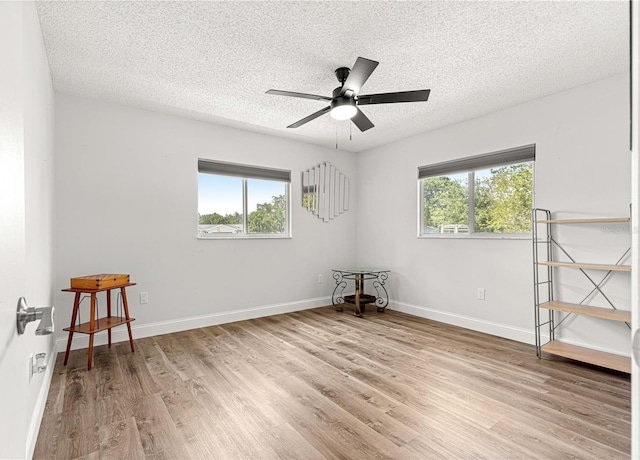 spare room featuring light wood finished floors, a textured ceiling, a ceiling fan, and baseboards