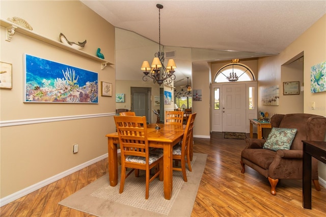 dining area with a chandelier, wood finished floors, baseboards, and lofted ceiling