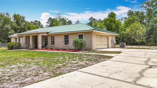 ranch-style house with central air condition unit, driveway, metal roof, a front yard, and an attached garage