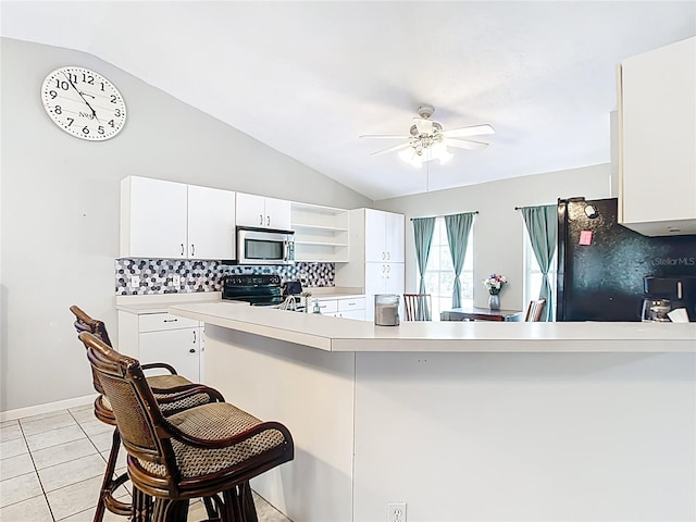 kitchen featuring stainless steel microwave, range with electric cooktop, freestanding refrigerator, decorative backsplash, and lofted ceiling