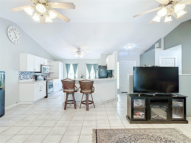 kitchen with appliances with stainless steel finishes, vaulted ceiling, light tile patterned flooring, a kitchen bar, and a ceiling fan