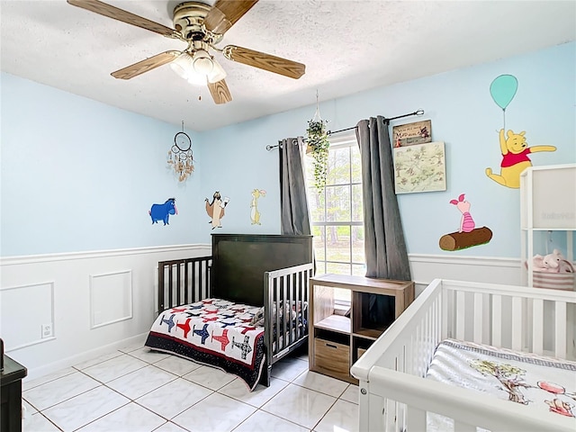 tiled bedroom featuring wainscoting, a textured ceiling, and ceiling fan