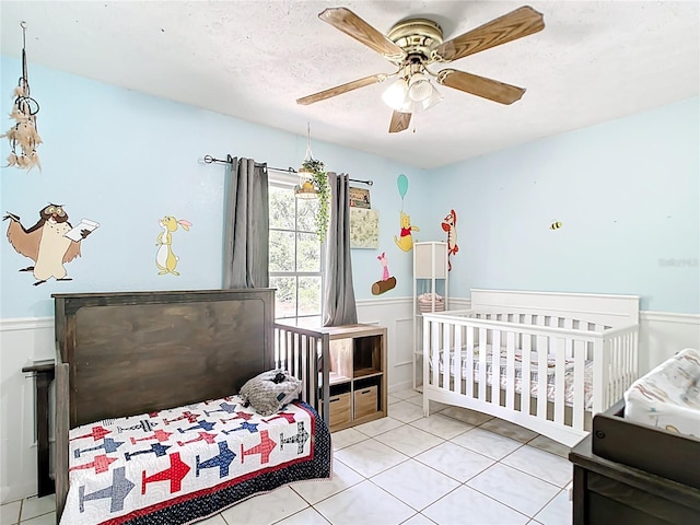 tiled bedroom featuring a wainscoted wall and a ceiling fan