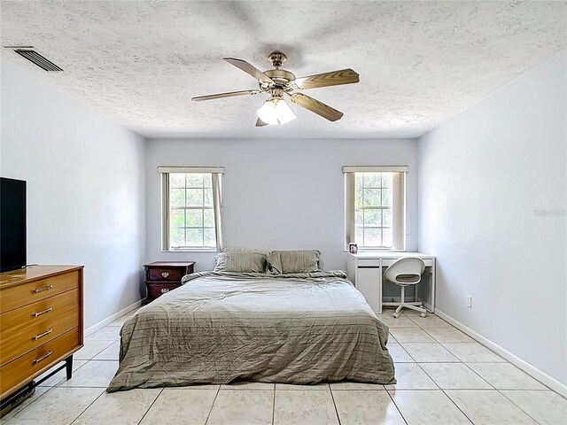 bedroom featuring multiple windows, a textured ceiling, a ceiling fan, light tile patterned floors, and baseboards