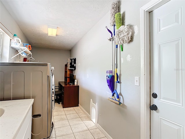 laundry room featuring a textured ceiling, light tile patterned flooring, baseboards, and washer / clothes dryer