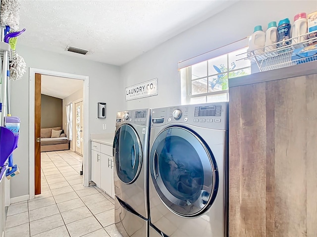 laundry room featuring washer and dryer, cabinet space, light tile patterned floors, and a textured ceiling
