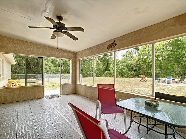 sunroom featuring a ceiling fan, lofted ceiling, and view of wooded area