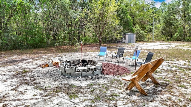 view of patio / terrace featuring an outdoor fire pit, a shed, an outbuilding, and a forest view