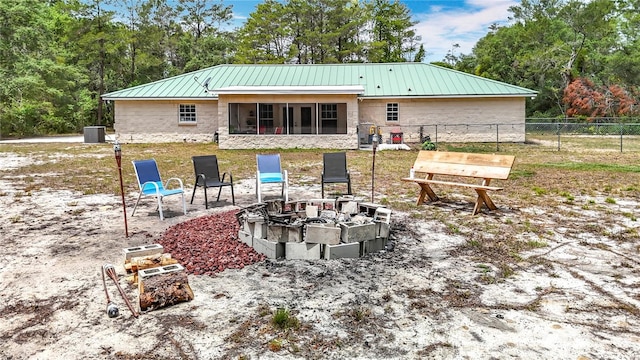 back of property featuring fence, a fire pit, a sunroom, and metal roof