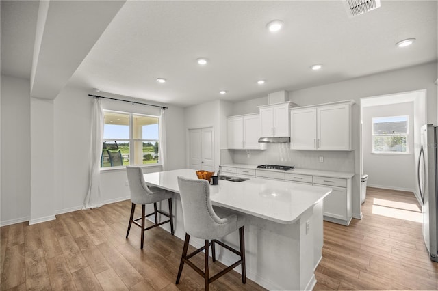7199 SW 60th Ln, Ocala, FL 34474 - kitchen featuring gas stovetop, under cabinet range hood, light countertops, light wood-style floors, and white cabinets