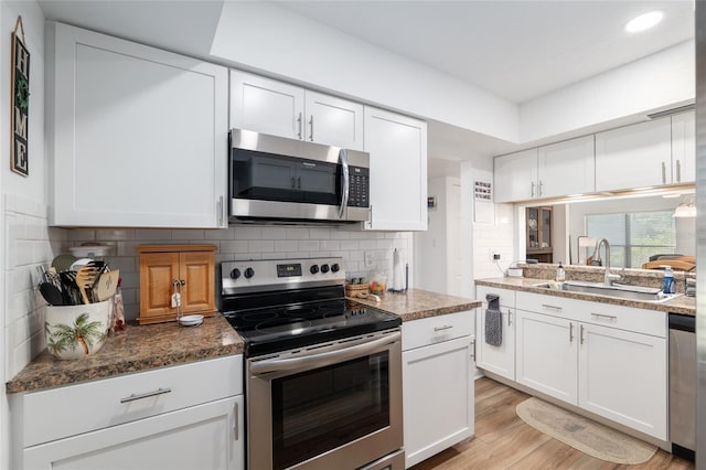 3815 NE 17th Street Cir, Ocala, FL 34470 - kitchen with stainless steel appliances, a sink, white cabinets, light wood-type flooring, and backsplash